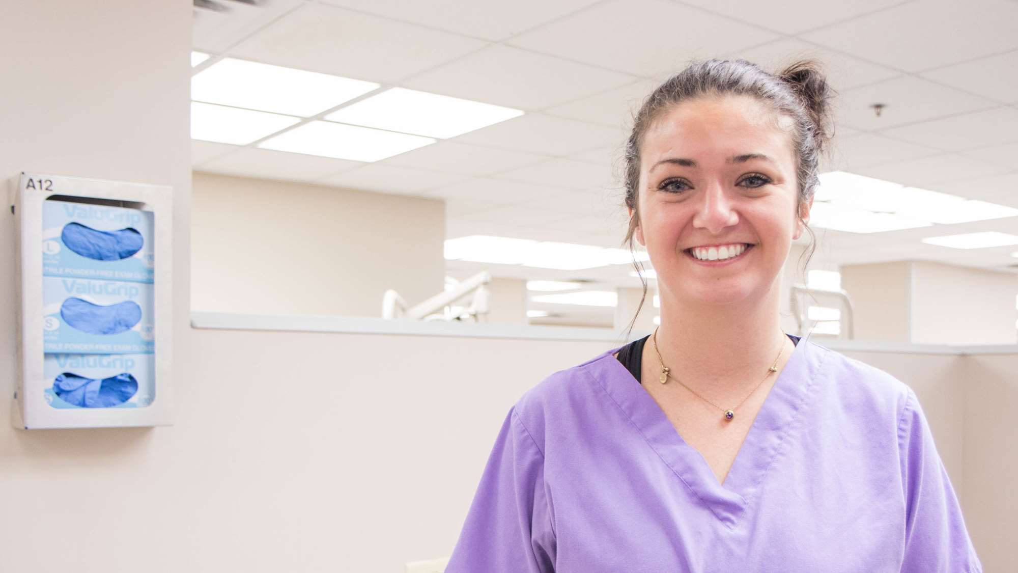 A young woman smiles, standing in a dental laboratory.