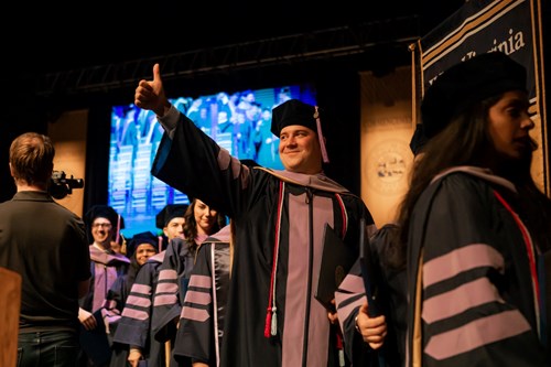 Jay Solensky, president of the Class of 2022 walks off the stage with a thumbs up in line with fellow dental school graduates.